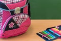 Pink girly school bag and pencil case on a desk against greenboard.