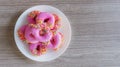 Pink glazed mini donuts in white plate on wooden table. Sweet food background