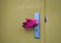 Pink glove covering a door handle of an ocre colored door of a c