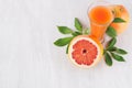 Pink grapefruits juice in elegant glass and grapefruits with green leaf on soft white wood background, copy space. Royalty Free Stock Photo