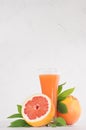 Pink grapefruits juice in elegant glass and grapefruits with green leaf on soft white wood background, copy space, vertical. Royalty Free Stock Photo