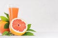 Pink grapefruits juice in elegant glass and grapefruits with green leaf on soft white wood background, copy space, closeup. Royalty Free Stock Photo