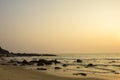 A pink gray clear sunset sky over the sea against a sandy beach with rocks in the ocean