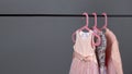 Pink and gray sequined luxury dresses for baby girls hang on hangers on a gray background