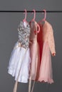 Pink and gray sequined luxury dresses for baby girls hang on hangers on a gray background