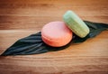 Pink and green color solid shampoo bars or conditioner bar on green leaf on wooden background.