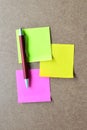 Pink, green, yellow note paper and red pen on wooden background. Royalty Free Stock Photo