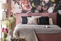 Pink and grey bed with cushions in patterned bedroom interior with flowers and lamp. Real photo