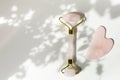 Pink Gua Sha massage tool. Rose Quartz roller. Gray shadow of the leaves on a white background. Facial skin care at home, anti-agi