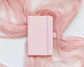 Pink hardcover notebook on tulle fabric on white table top view, textbook mockup