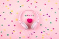 Pink headphones and heart with word MUSIC and multicolored letter symbols on pink background. Minimal Music concept. Top view.