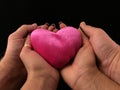 Pink heart on the palms of a woman and a man. Two pairs of hands hold a heart, on a black background. Concept: take care of love,