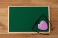 The pink heart-shaped box is decorated with ribbon and black eyeglasses on a green chalkboard. Royalty Free Stock Photo