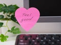 Pink heart shaped paper note with words Feel Good on it sticked on to a monitor at an office workplace Royalty Free Stock Photo