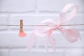 Pink heart with silk bow hanging from a rope with clothespins on a white background.