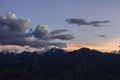 A pink horizon under heavy gray clouds in the dark blue sky of sunset over the dark silhouettes of mountains with snowy peaks