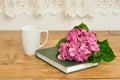 A pink hydrangea, a green story book and a mug