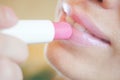 Pink hygienic lipstick in fingers applies to lips with a smile
