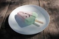 Pink ice cream popsicle in the shape of watermelon on a white plate. Vintage wooden table background with copy space. Royalty Free Stock Photo