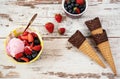 Pink Ice Cream served with berries - strawberries and blueberries in a yellow bowl. Waffle cones with chocolate. Light Rustic Wood