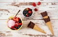 Pink Ice Cream served with berries - strawberries and blueberries in a yellow bowl. Waffle cones with chocolate. Light Rustic Wood