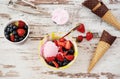 Pink Ice Cream served with berries - strawberries and blueberries in a yellow bowl. Waffle cones with chocolate. Light Rustic Wood