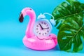 Pink inflatable flamingo on blue background with monstera leaves and clock. Royalty Free Stock Photo