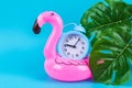 Pink inflatable flamingo on blue background with monstera leaves and clock Royalty Free Stock Photo