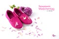 pink kid shoes, a flower and petals isolated on a white background, german text Internationaler Maedchentag, that means