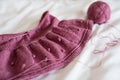 A pink knitted skirt lies on the bed, white background from a white sheet, threads of wool and a skein of yarn lie nearby