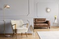 Pink lamp next to armchair in grey apartment interior with gold leaf and bright carpet