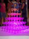 Pink light in champagne glasses standing in a tower filled party close up