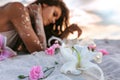 Pink lilies lying on sand foreground and young beatiful woman lying on sand at background on the beach at sunset