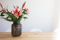 Pink lily flowers in a vase on a wooden table in the interior against a white wall in modern room Royalty Free Stock Photo