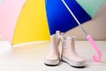 Pink little children rubber boots stand under colorful umbrella.
