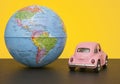Pink little retro car with world globe sphere. Travel concept. Planning season vacations. back view Royalty Free Stock Photo