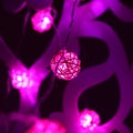 Pink magenta Rattan ball garland on patterned wall. New Year`s garland. Christmas led lights on dark background. Blurred glowing Royalty Free Stock Photo