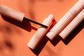 Pink makeup brush for eyeliner lies on an open tube, closed tubes of cosmetics, mascara, lip gloss, pink lipstick on a peach backg