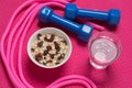 on the pink mat for fitness are dumbbells, a glass of water, a jump rope and a plate with muesli, concept of sport