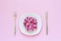 Pink measuring tape lying on plate in the form of spaghetti, knife and fork on pink background Royalty Free Stock Photo