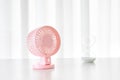 Pink metal mini fan and a sand hourglass on a white table