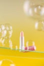 Pink moisturizing hygienic lipstick on a glass shelf on a yellow background surrounded by soap bubbles.