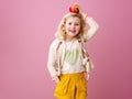 Child isolated on pink background holding an apple on head