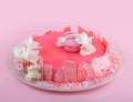 Pink mousse cake with mirror glaze decorated with macaroons, flowers for Happy Birthday on pink holiday background. Holiday cake