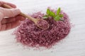 Pink natural bath salt on white wooden background with mint leaf and human hand with spoon