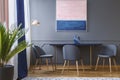 Pink and navy blue painting above table and grey chair in dining room interior. Real photo Royalty Free Stock Photo