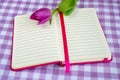 Pink notepad with lined paper and one purple tulip on a white purple checkered textile background. Greeting card with copy space Royalty Free Stock Photo