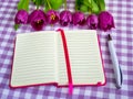 Pink notepad with lined paper, white ballpoint pen and a row of purple tulips on a white purple checkered textile background. Royalty Free Stock Photo