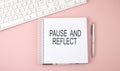 Pink office desk with keyboard and notebook with text PAUSE AND REFLECT Royalty Free Stock Photo