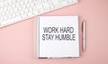 Pink office desk with keyboard and notebook with text WORK HARD STAY HUMBLE Royalty Free Stock Photo